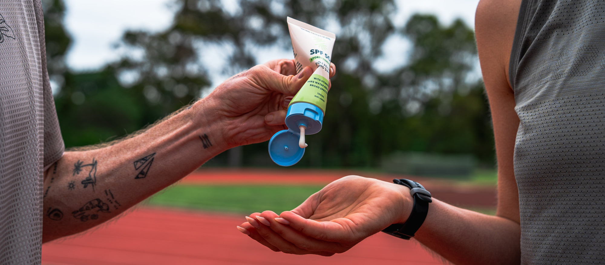 Runner applying Sun Motion SPF50+ sports sunscreen to another runner's hand outdoors on a track