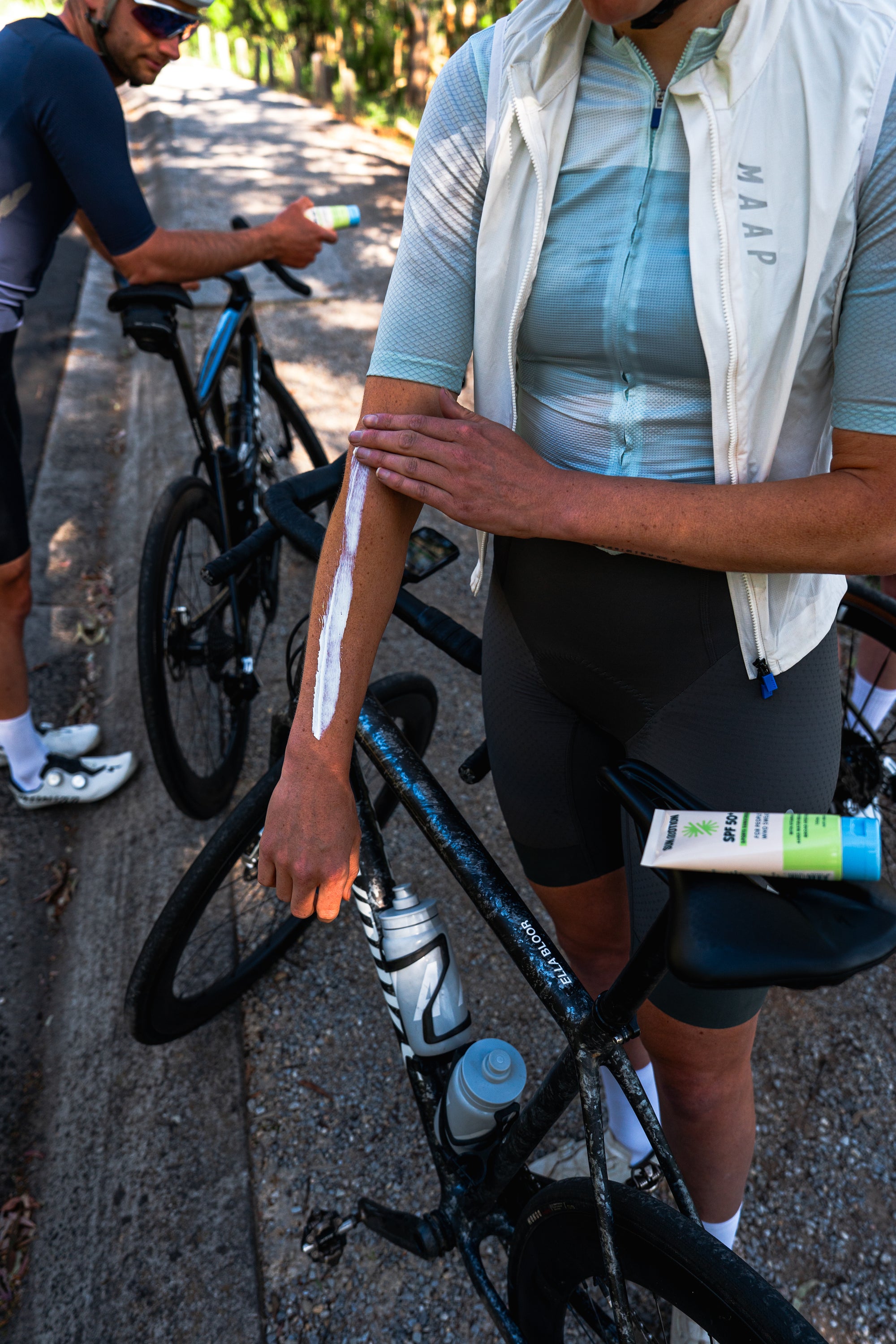 Cyclist applying sunscreen on arm with another cyclist in the background