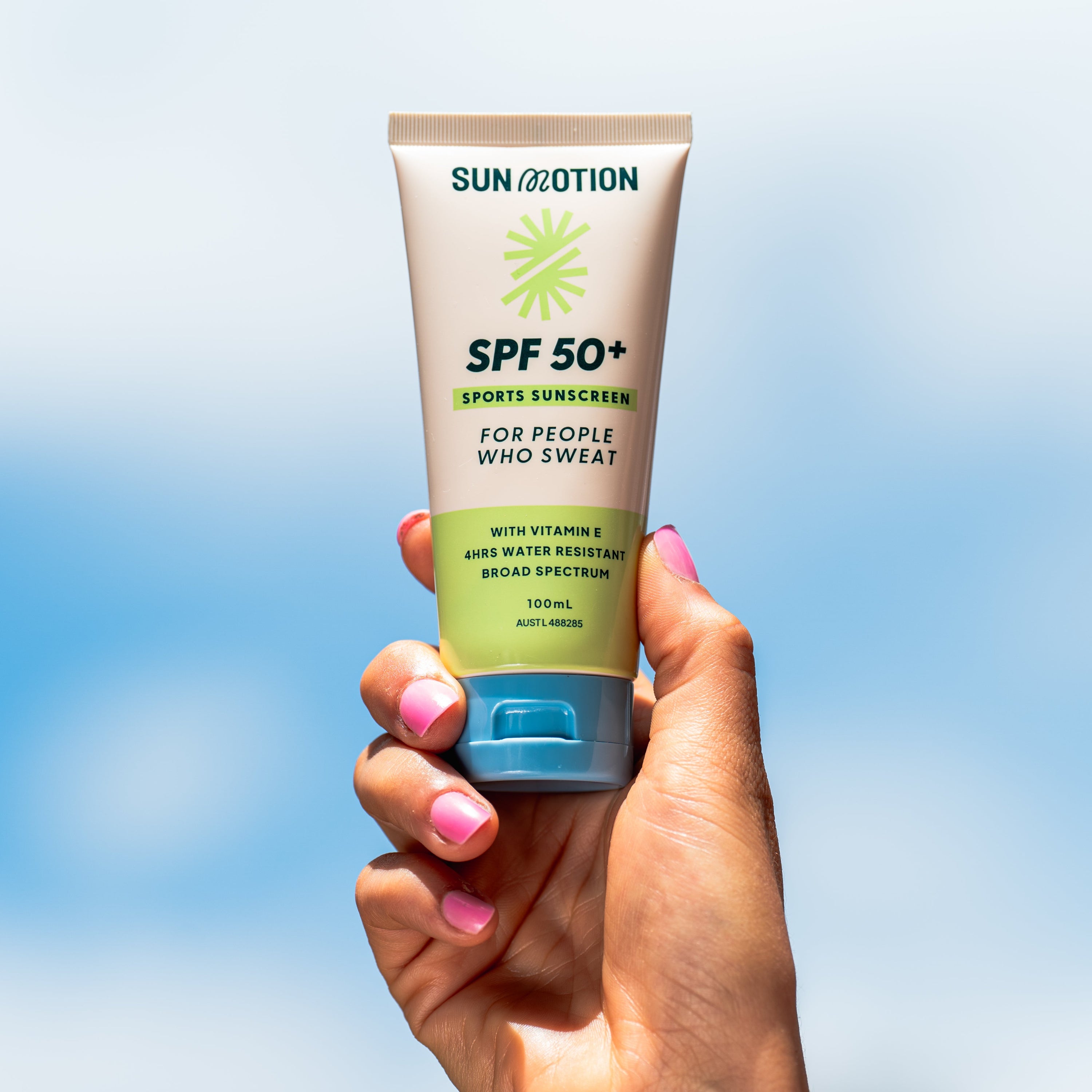 Hand holding a tube of Sun & Motion SPF 50+ sunscreen against a clear blue sky.